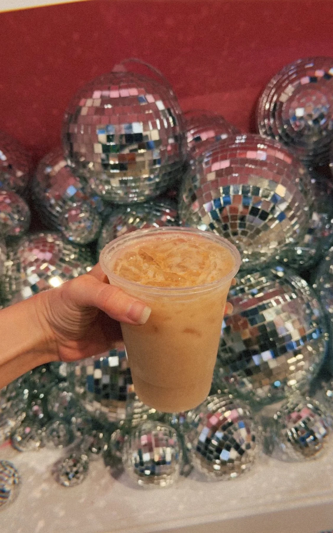 An iced coffee held beside mirrored decorations at a pop-up