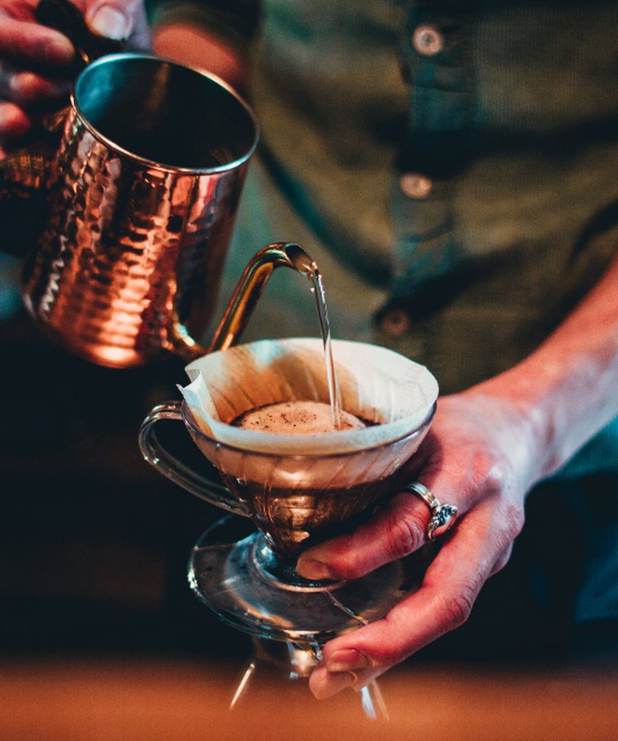 Barista pouring from a copper kettle into a pour-over